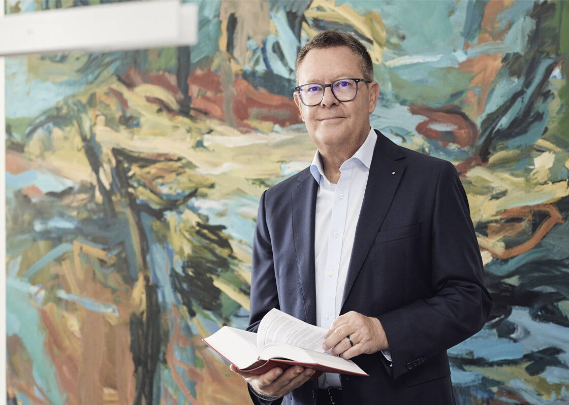 Mann mit Brille und Anzug. Trägt ein Gesetzbuch in der Hand. 