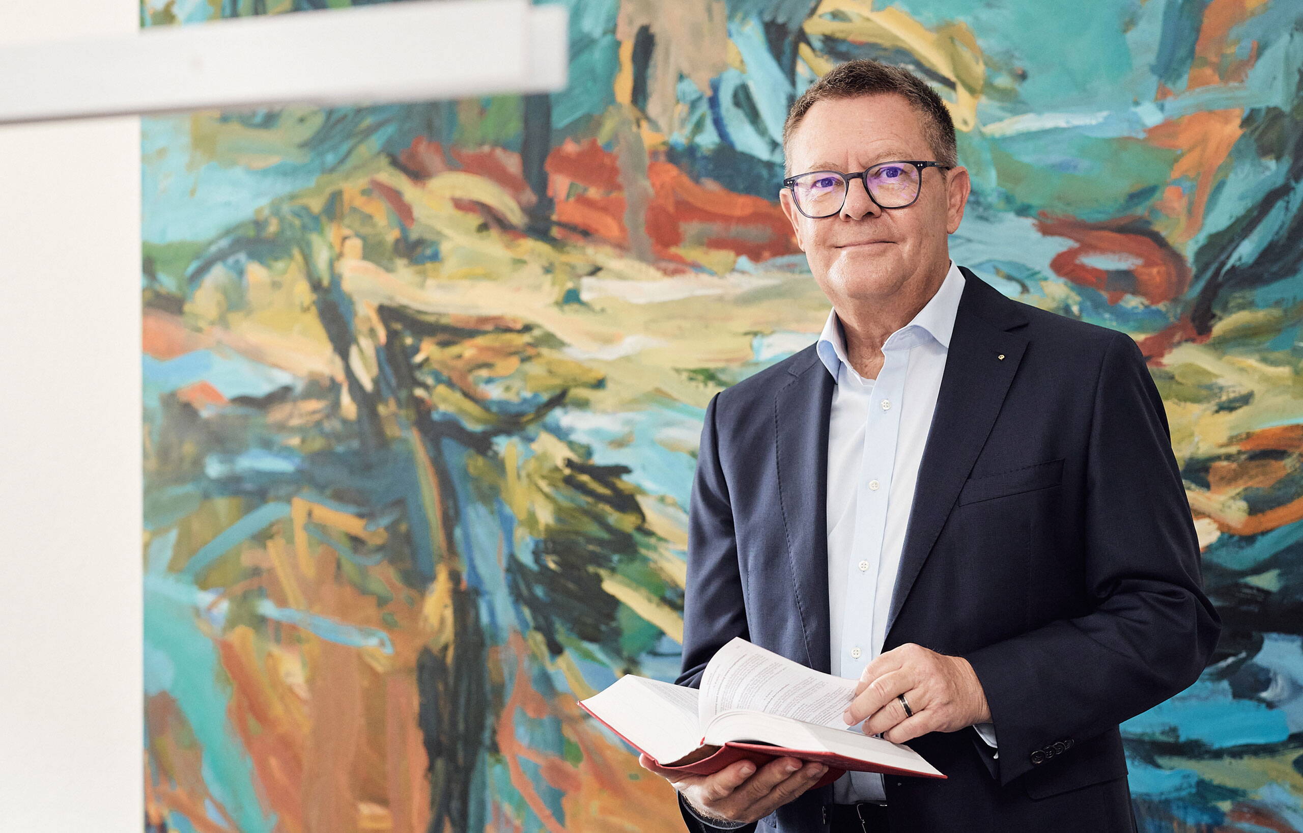 Mann mit Brille und Anzug. Trägt ein Gesetzbuch in der Hand. 