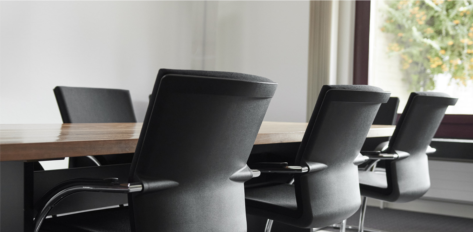 grafkrummenacher_teaser_karriere.jpg Langer, leerer Sitzungstisch mit schwarzen Bürostühlen.