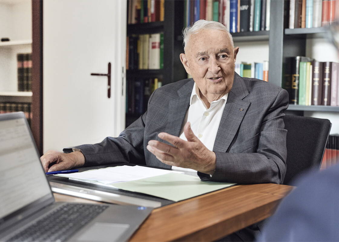 Älterer Mann mit Jaquet der am Tisch mit einem Kunden eine Besprechung hat