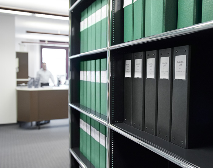grafkrummenacher_kanzlei_rechtsfragen.jpg Bücherregal mit grünen und schwarzen Aktenordnern.